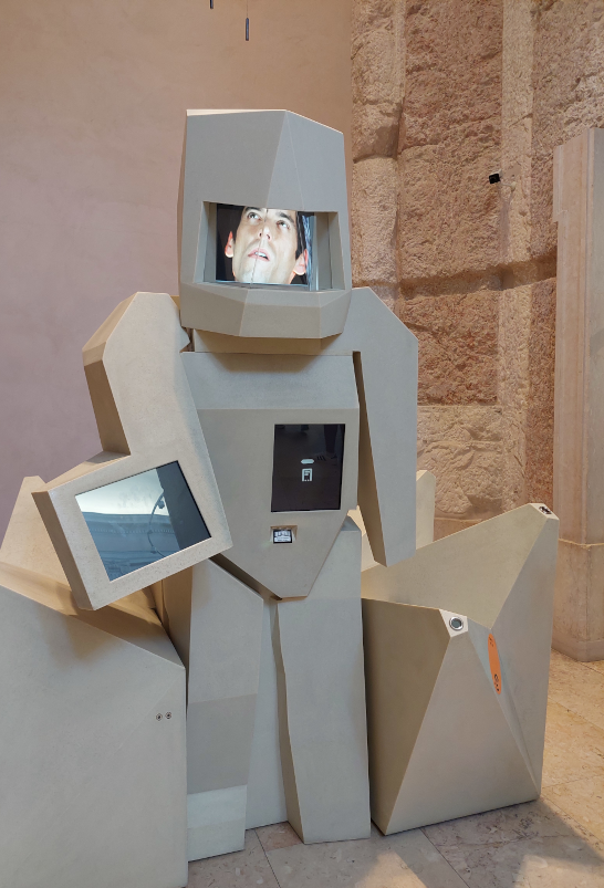 Museum exhibit that looks a bit like a stone golem, but its face is a screen.